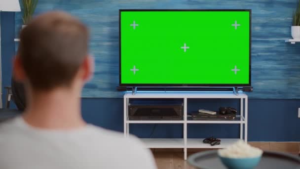 Over schouder uitzicht van de mens kijken film op tv met groen scherm ontspannen met kom popcorn — Stockvideo