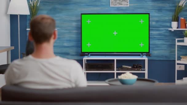 Mężczyzna siedzi na kanapie patrząc na zielony ekran w telewizji relaksujący oglądanie filmu w nowoczesnym salonie — Wideo stockowe