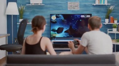 Kız arkadaşı patlamış mısır yerken ve ona tavsiye verirken oyuncu televizyonda birinci şahıs nişancı konsolu oynuyor.