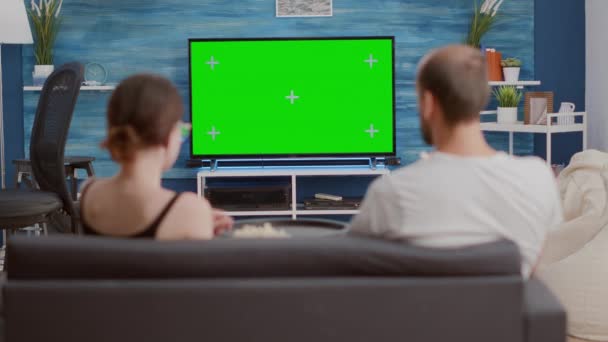 Trípode estático de la pareja tomando un aperitivo mientras mira la televisión de pantalla verde viendo una película — Vídeos de Stock