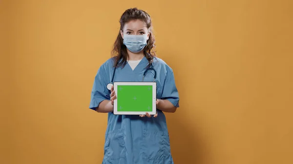 녹색 화면에 병원 유니폼을 입고 열렬 한 보호 마스크를 쓴 여자 의사가 태블릿 컴퓨터를 들고 있는 모습 — 스톡 사진