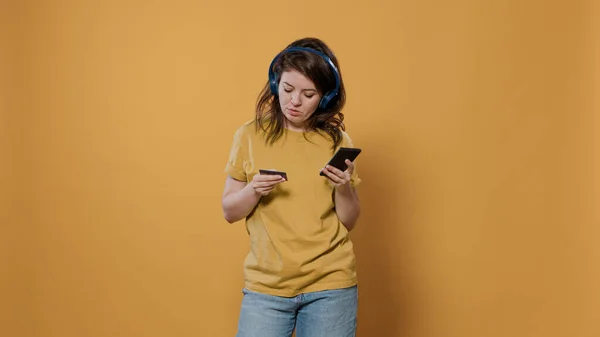 Mujer sosteniendo teléfono inteligente escribiendo datos de la tarjeta de crédito haciendo compras en línea mientras escucha música — Foto de Stock