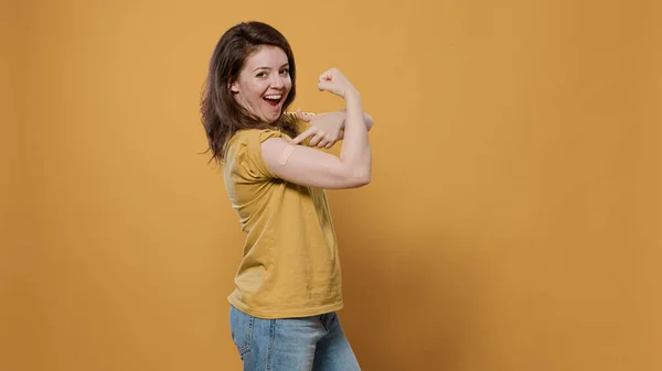 Retrato de una mujer sonriente levantando la manga y mostrando una tirita después de la vacuna covid o gripe flexionando los bíceps del brazo —  Fotos de Stock