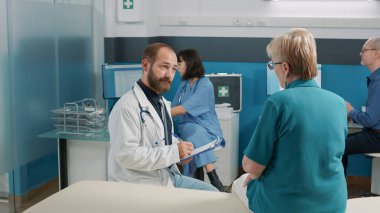 Erkek doktor not alıyor ve yaşlı insana danışıyor.