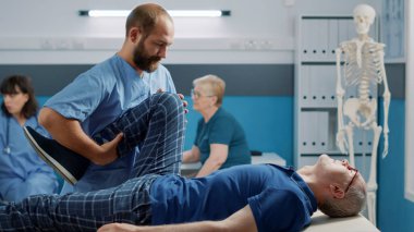 Erkek osteopat bacakları kırıyor, kemikleri kırıyor ve yaşlı adamın kaslarını esnetmesine yardım ediyor.