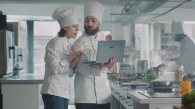 Kadın ve erkek mutfakta yemek tarifi yapmak için dizüstü bilgisayar kullanıyor.