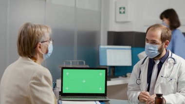 Emekli kadın ve doktor yeşil ekranlı dizüstünü inceliyor.