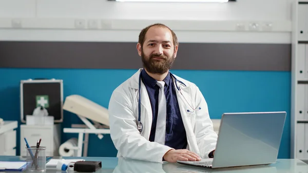 Portrait of male physician wearing white coat and using laptop — Stock Photo, Image