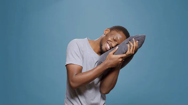 Modelo exausto usando travesseiro para tirar uma soneca sobre fundo azul — Fotografia de Stock