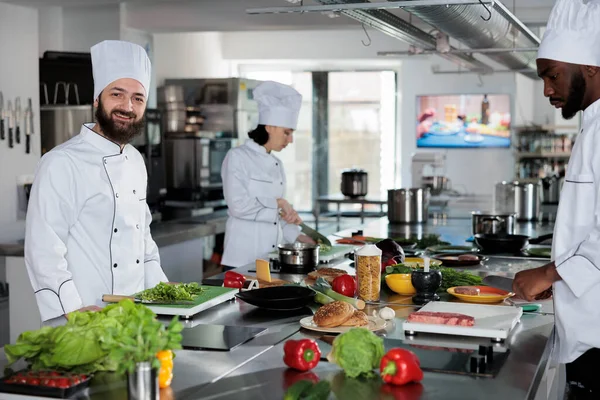 Chef jefe sonriente positivo en el espacio de cocina profesional del restaurante preparando comida gourmet con ingredientes deliciosos. — Foto de Stock