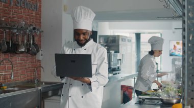 Afro-Amerikan fırıncısı yemek pişirmek için laptop ekranına bakıyor.