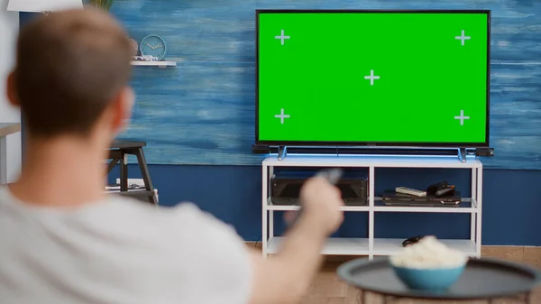 Por encima de la vista del hombro del hombre cambiando de canal mientras mira la pantalla verde en la televisión y sentado en el sofá — Foto de Stock