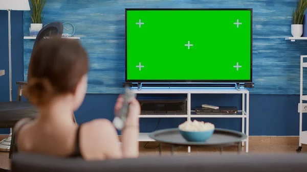 Trípode estático de la mujer joven cambiando canales mientras mira la pantalla verde en la televisión — Foto de Stock