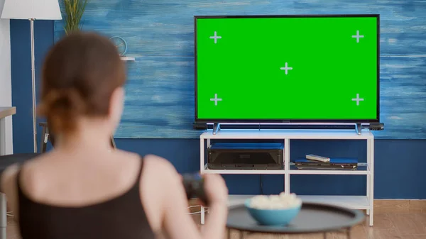 Przez ramię widok młodej kobiety grającej w konsolę gier wideo z kontrolerem bezprzewodowym na zielonym ekranie telewizora — Zdjęcie stockowe