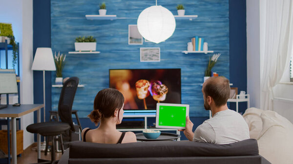 Couple on sofa watching online show using streaming app on digital tablet with green screen