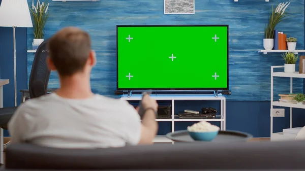 Kanepede oturan adam TV 'de yeşil ekrana bakıyor ve kanal değiştiriyor. — Stok fotoğraf