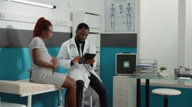 Doğum uzmanı çocuk bekleyen hastaya danışmak için dijital tablet kullanıyor.