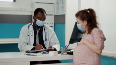 Sağlık sigortası hakkında konuşan, yüz maskeli ve hamile bir kadın.