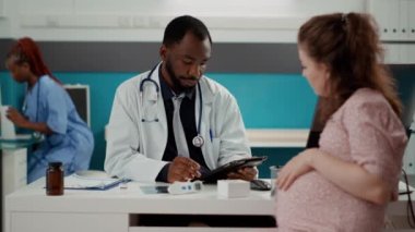 Genel pratisyen anne adayıyla istişare için dijital tablet kullanıyor.