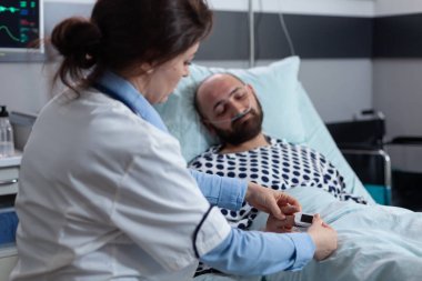 Doktor, burun kanülü oksijene bağlı uyuyan hastanın parmağına nabız oksimetresi takıyor.