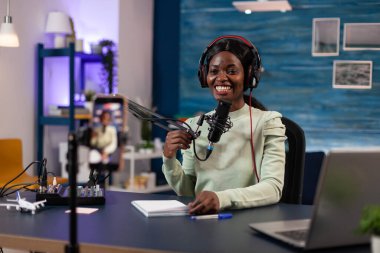 Kulaklıklı, prodüksiyon mikrofonuna konuşan podcast yapımcısı kadın