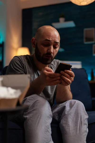 Hombre deprimido utilizando el teléfono inteligente para navegar por Internet en casa —  Fotos de Stock