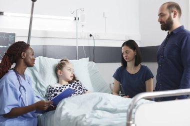 Endişeli genç aileler, Afrikalı Amerikalı hemşirelerin hasta küçük bir kızın konsültasyon sonuçları hakkında konuşmalarını dinliyor..