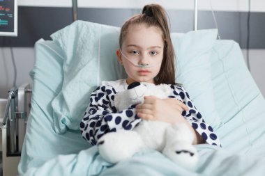 Hasta çocuk oyuncak ayıyı tutuyor ve çocuk kliniğinde tek başına dinlenirken oksijen tüpü takıyor..