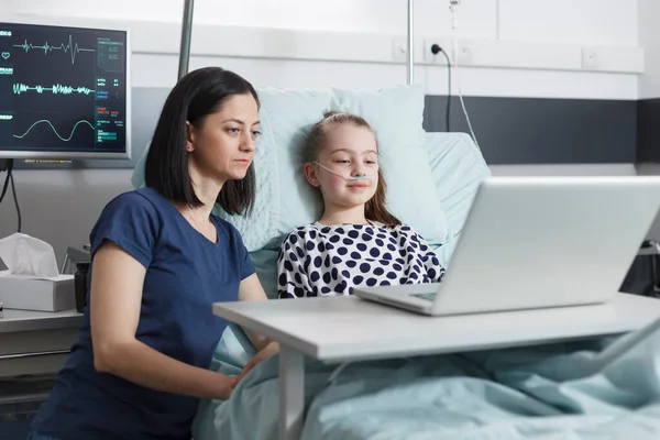 Ung mor och leende sjuk liten flicka tittar på roliga videor på laptop. — Stockfoto