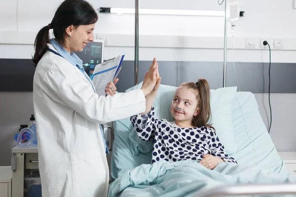Healthcare clinic pediatrician expert high-fiving ill little girl while in patient recovery ward room. — Stock Photo, Image