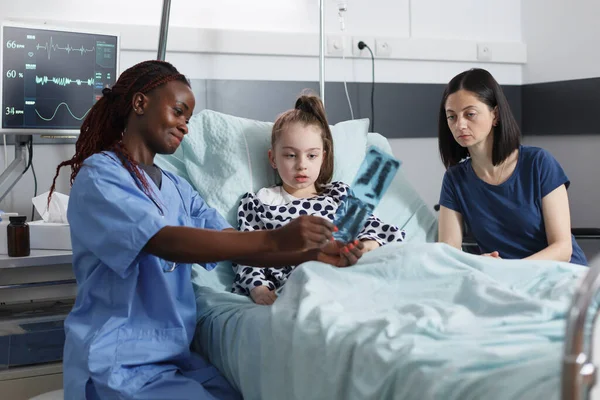 Gezondheidszorg kliniek pediatrische glimlachende verpleegkundige tonen onwel klein meisje radiografie resultaten. — Stockfoto