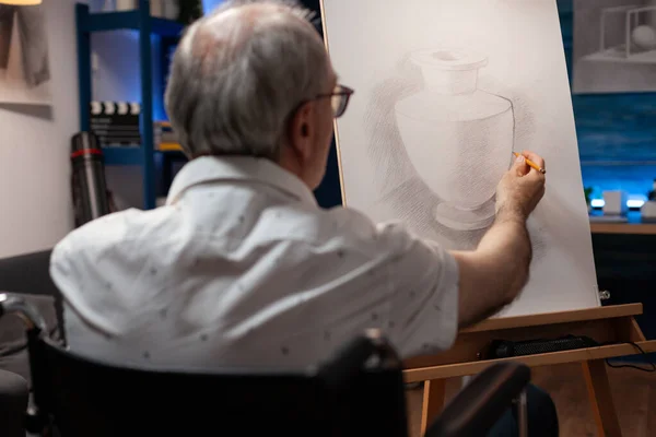 Retrato de close-up de artista homem sênior usando cadeira de rodas esboçando desenho a lápis original de vaso no cavalete — Fotografia de Stock