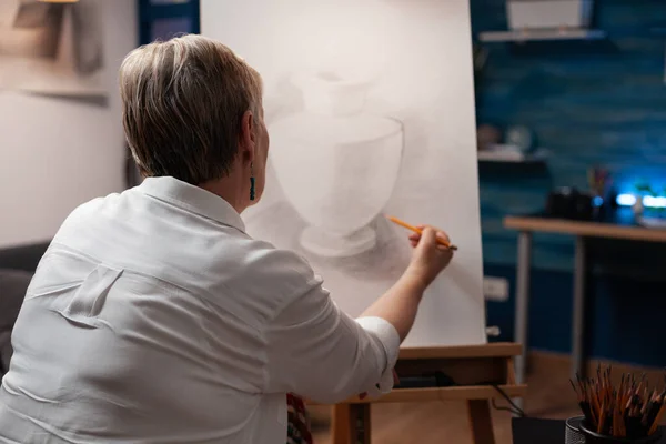 Вид через плечо пожилой женщины, рисующей органальный шедевр острым карандашом на бумажном наброске — стоковое фото