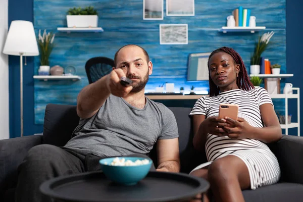 Casal adulto multiétnico sentado no sofá e assistindo programas de televisão — Fotografia de Stock