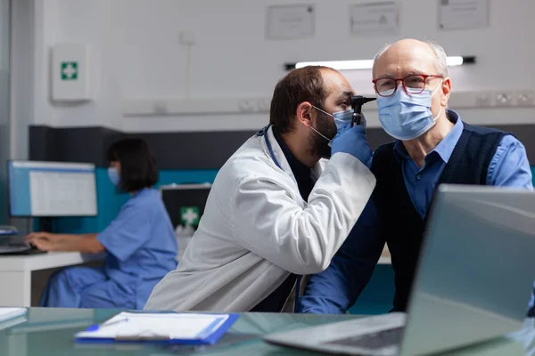 Specialist using otoscope to do ear examination on elder man