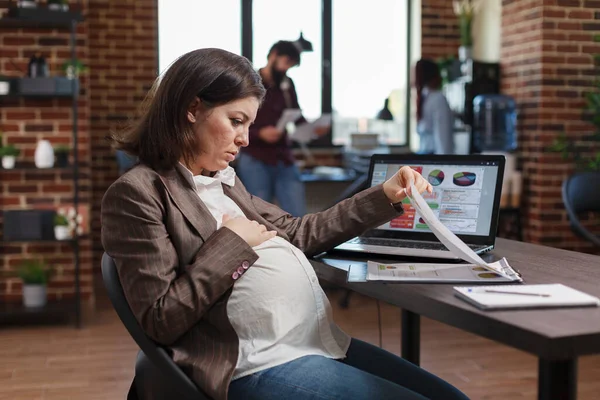 Mulher grávida questionando gráficos de dados e resultados de análises de negócios enquanto se senta na mesa do escritório. — Fotografia de Stock