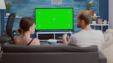 Çift kanepede oturup televizyon izler yeşil ekran düz ekran TV 'de en sevdiği program hakkında konuşur ve zap yapar.