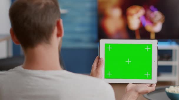 Close-up de homem segurando tablet digital com tela verde assistindo conteúdo de vídeo on-line sentado no sofá — Vídeo de Stock