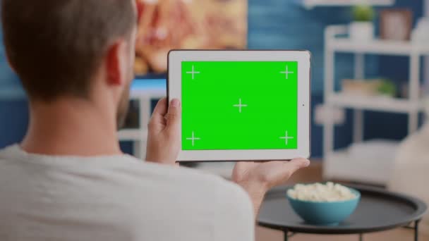 Primer plano del hombre sosteniendo la tableta digital con pantalla verde viendo webinar sentado en el sofá — Vídeos de Stock