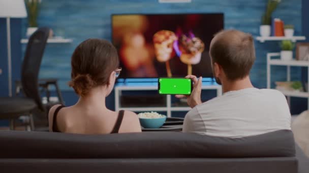 Tripé estático tiro de homem segurando smartphone com tela verde assistindo conteúdo de vídeo online com namorada — Vídeo de Stock