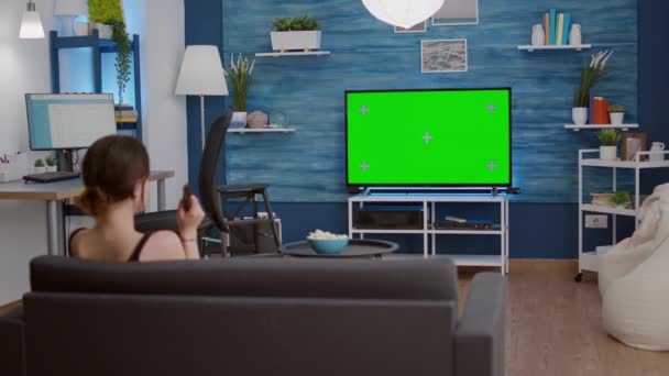 Trípode estático disparo de mujer joven zapping tv lookin para el programa favorito mientras mira la pantalla verde — Vídeo de stock