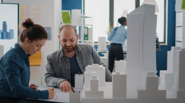 İnşaat modelini ve planlarını analiz eden bir grup iş arkadaşı, inşaat planlarını tasarlamak için masa üzerinde plan yapıyor.