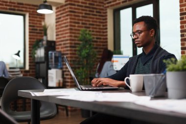 Reklam şirketi çalışanı iş laptopu kullanarak proje pazarlama stratejisi üzerinde çalışıyor.