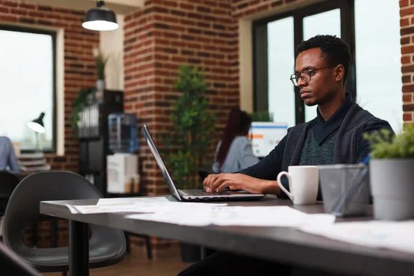 Reklam şirketi çalışanı iş laptopu kullanarak proje pazarlama stratejisi üzerinde çalışıyor.