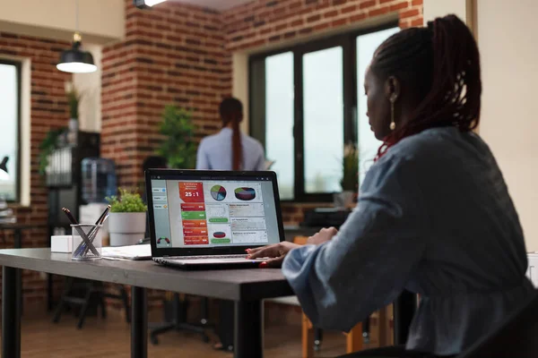 Empresária afro-americana trabalhando no gráfico de gestão de negócios ao usar laptop de trabalho. — Fotografia de Stock