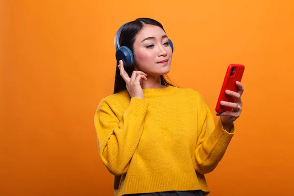 Relaxado amigável bonito asiático mulher ouvir música no áudio streaming plataforma enquanto usando smartphone dispositivo. — Fotografia de Stock