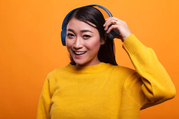 Bonito alegre positivo asiático pessoa pára de ouvir música para falar com o companheiro enquanto no fundo laranja. — Fotografia de Stock