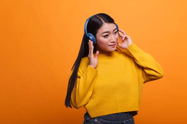 Relaxado amigável bonito asiático mulher ouvir música no áudio streaming plataforma usando fones de ouvido sem fio. — Fotografia de Stock