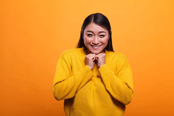 Aşırı neşeli Asyalı kadın turuncu arka planda canlı süveter giyerken yürekten gülümsüyor.. — Stok fotoğraf