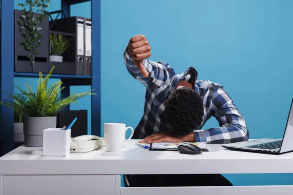 Sleepy tired man showing dislike gesture while resting head on desk. — Stock Photo, Image